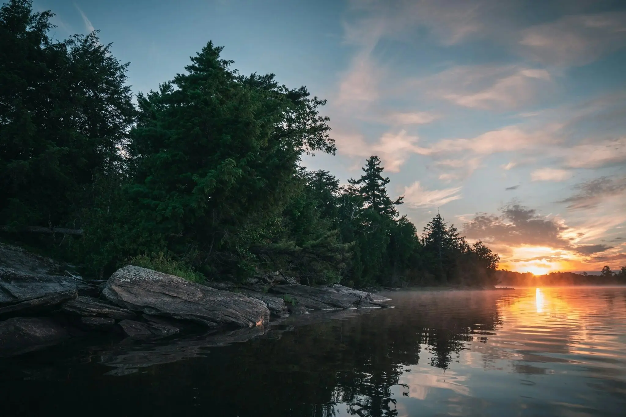Sunset over tranquil lake with trees.