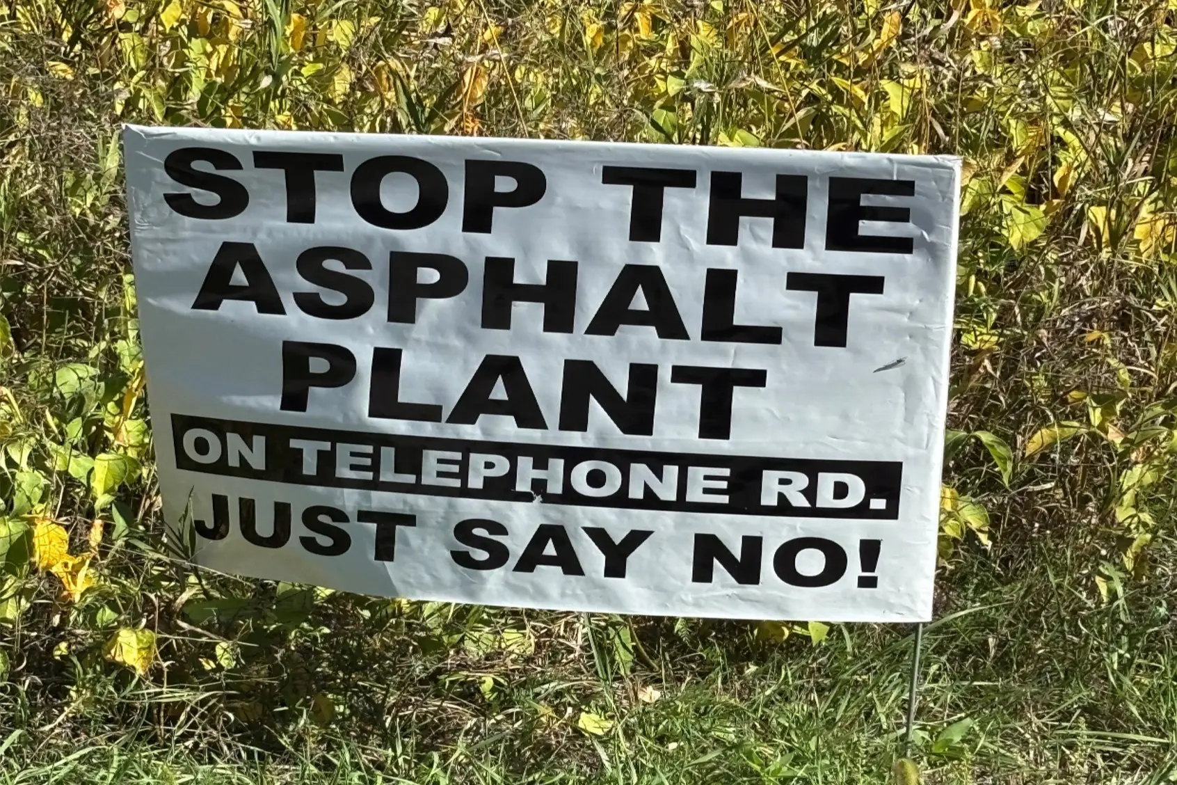 Protest sign urging to stop the asphalt plant near a telephone pole.