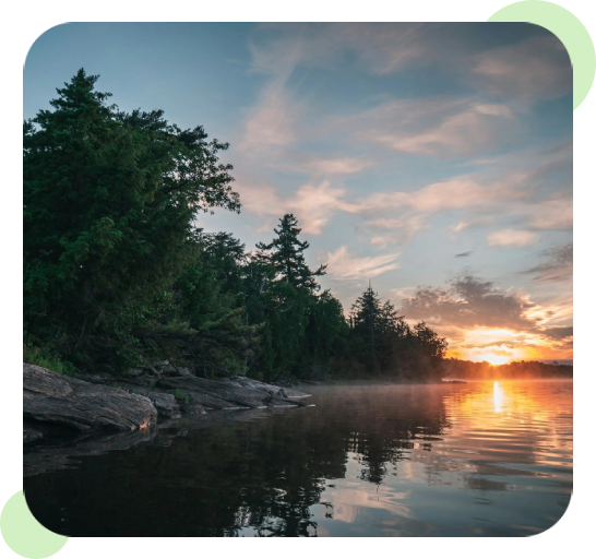 Sunset over a calm lake bordered by trees and rocks.