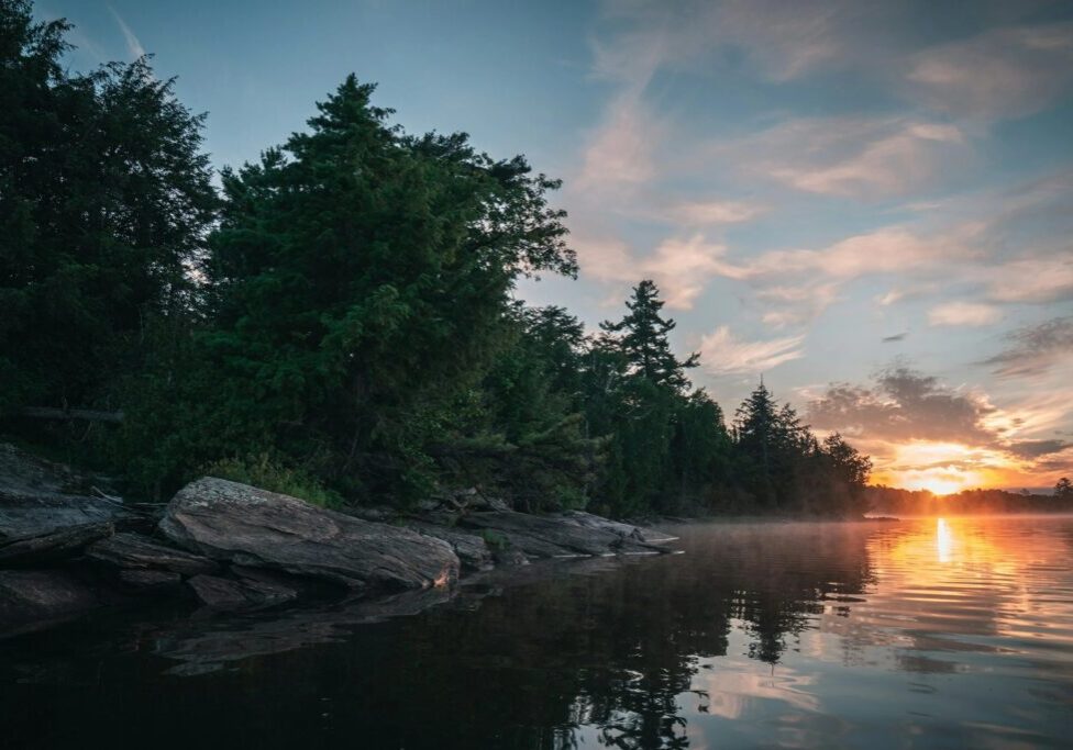 Sunset over tranquil lake with trees.
